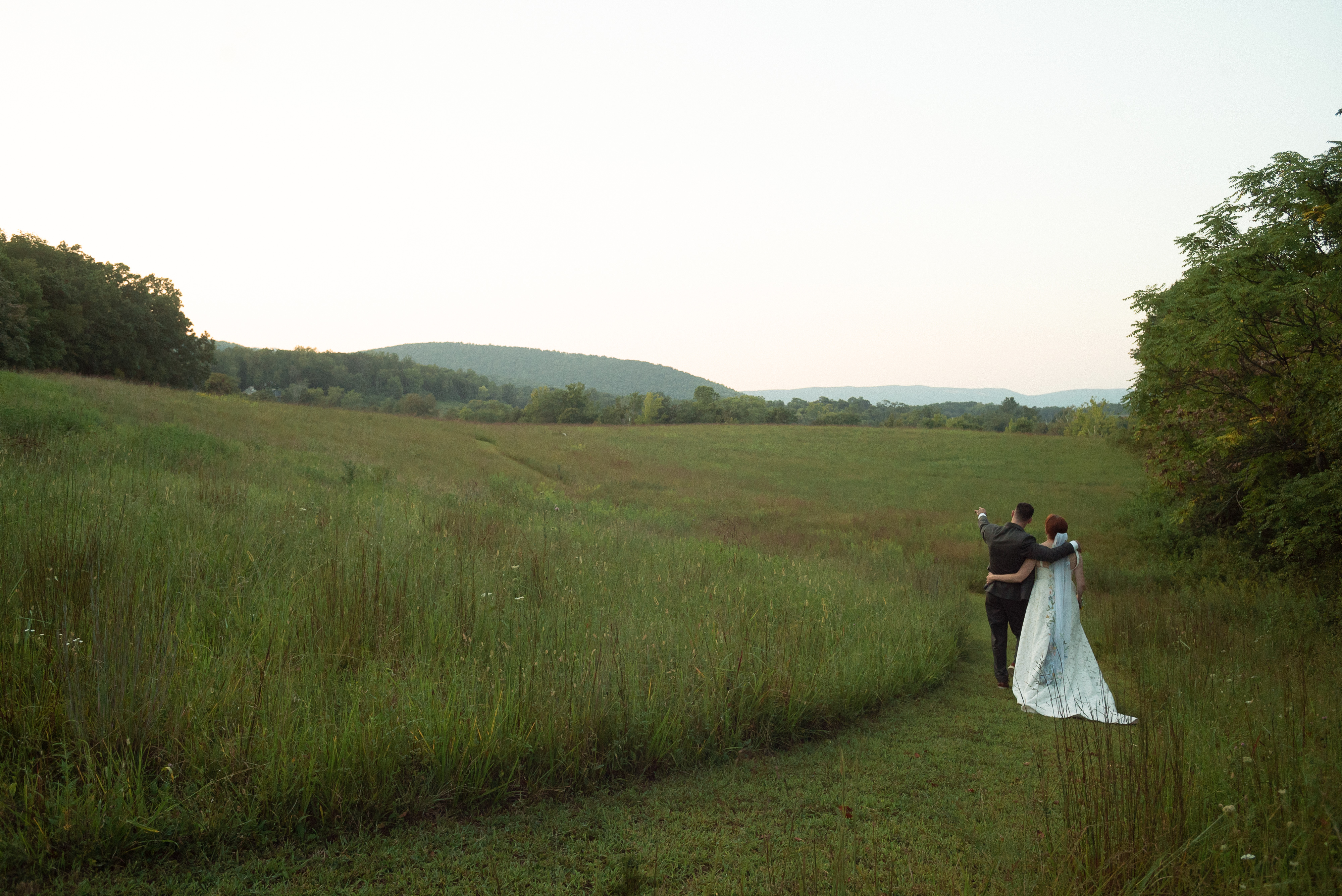 bride and groom walking in rural field at the indigo house in afton virginia with mountains backdrop - documentary style wedding photography in virginia -taken with vintage 28mm wide angle lens film look