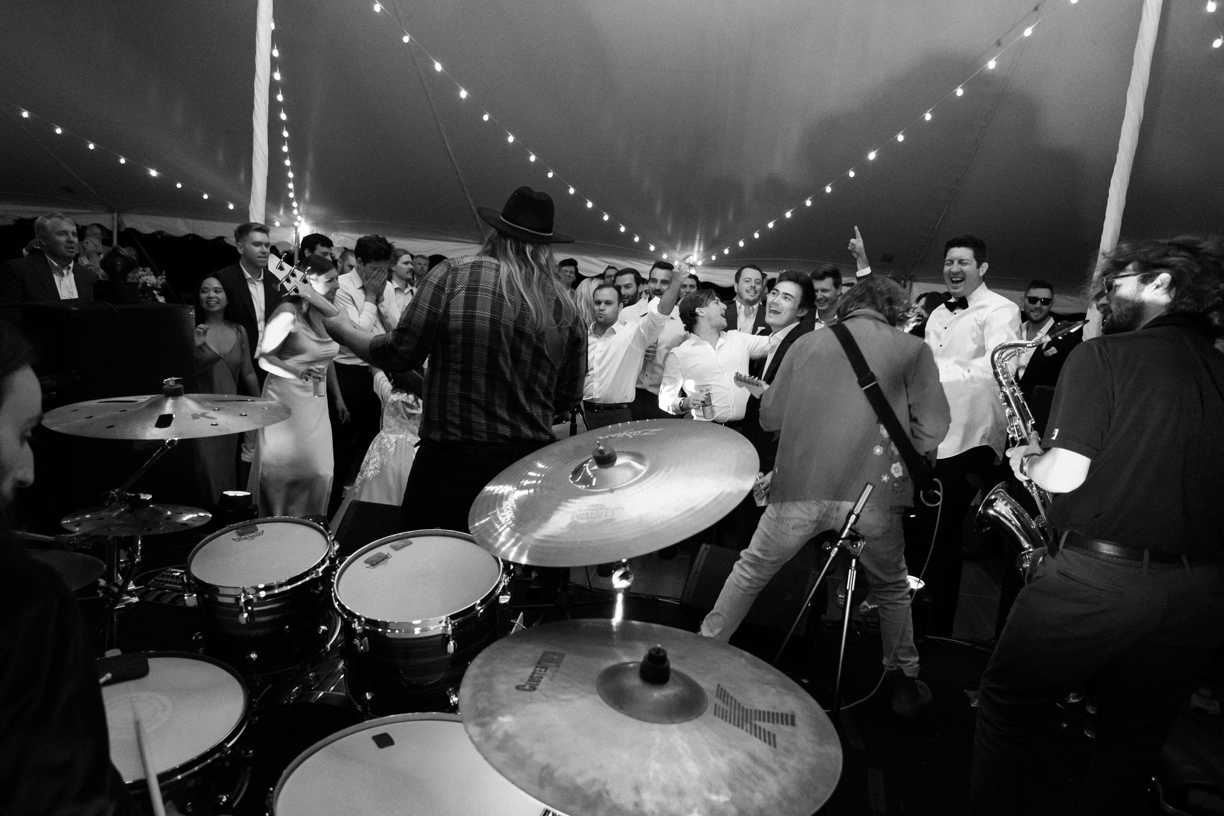 live band playing at a wedding reception shot on wide angle lens as viewed behind drummer - photojournalistic style wedding photo in black and white