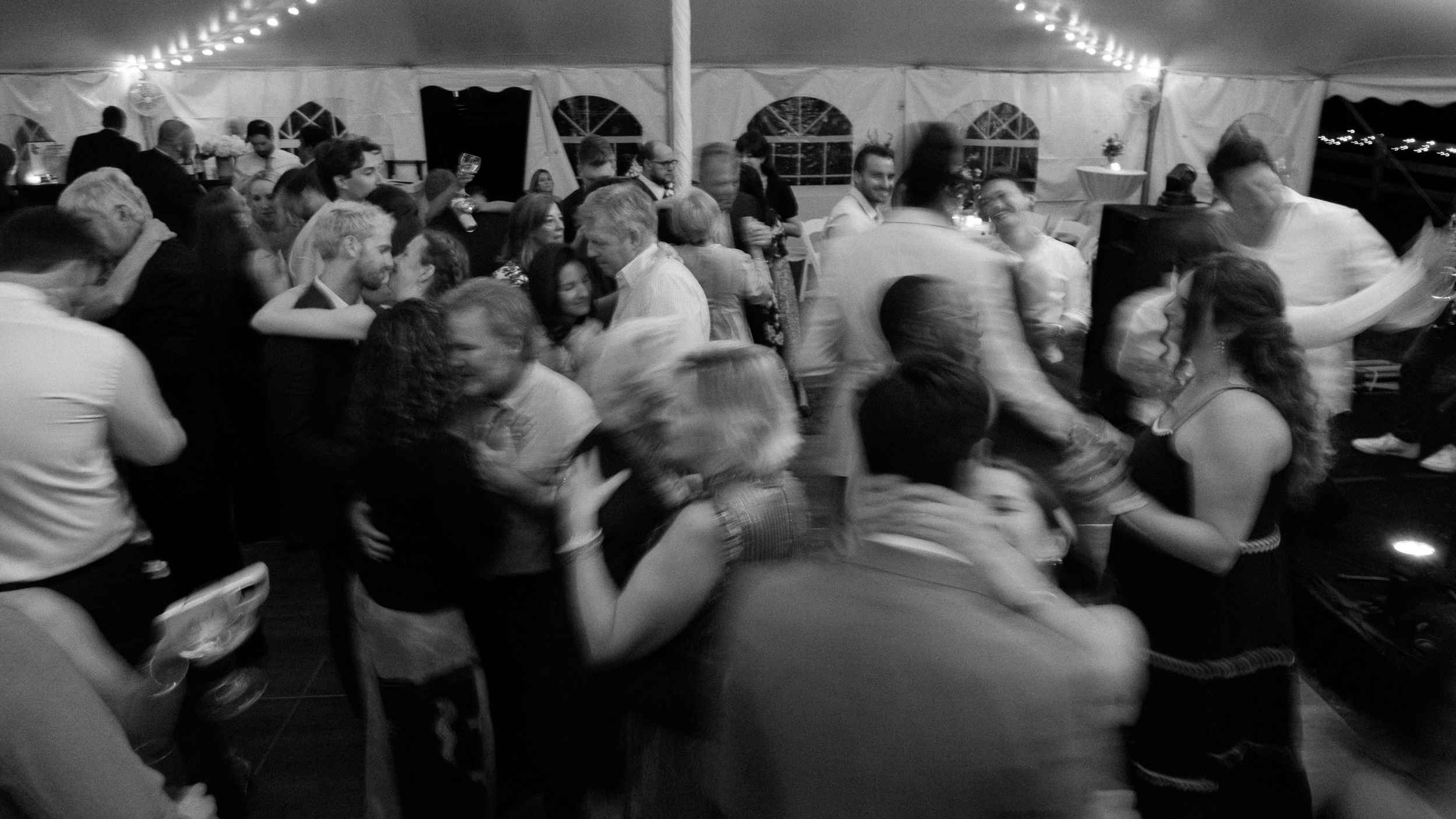 wide angle black and white photograph of wedding guests slow dancing at reception intentionally blurry to show movement - documentary style wedding photography