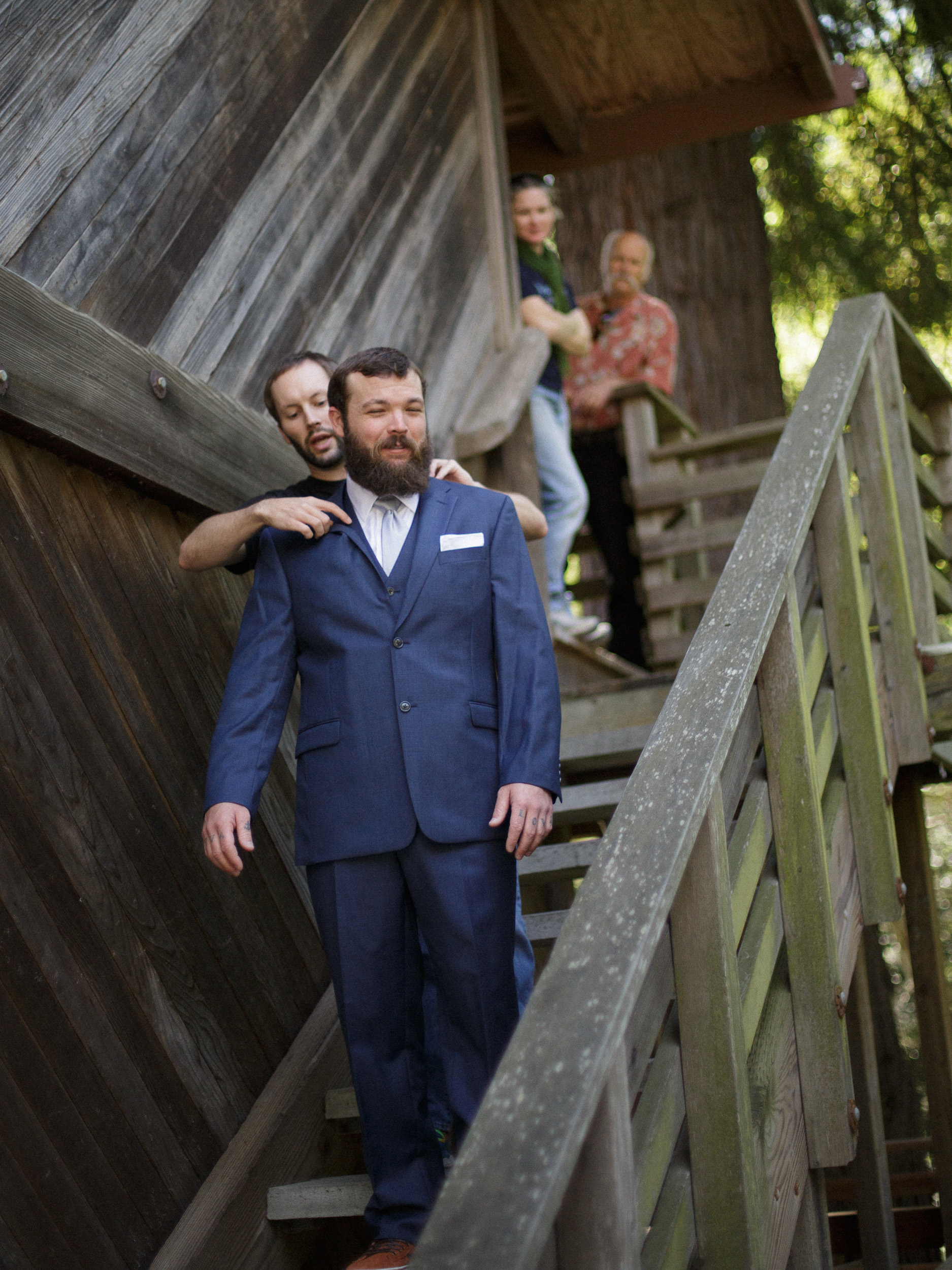 groom getting his jacket fixed as he descends staircase next to the big sur bakery - - big sur california wedding - laid back wedding in big sur california - true to life colors