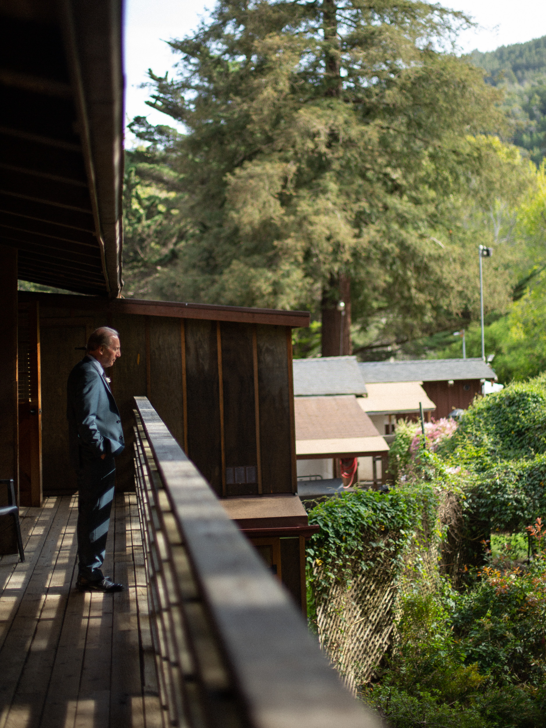 father of bride looks over ceremony location from balcony at big sur river inn - big sur california wedding - laid back wedding in big sur california - true to life colors