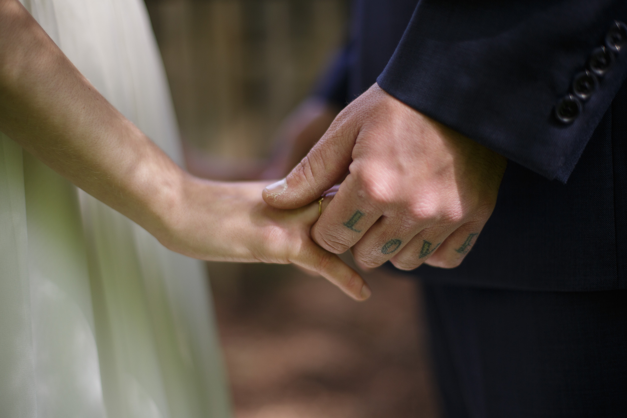 wedding day closeup of groom's "love" tattoo as he holds hands with bride - big sur california wedding - laid back wedding in big sur california