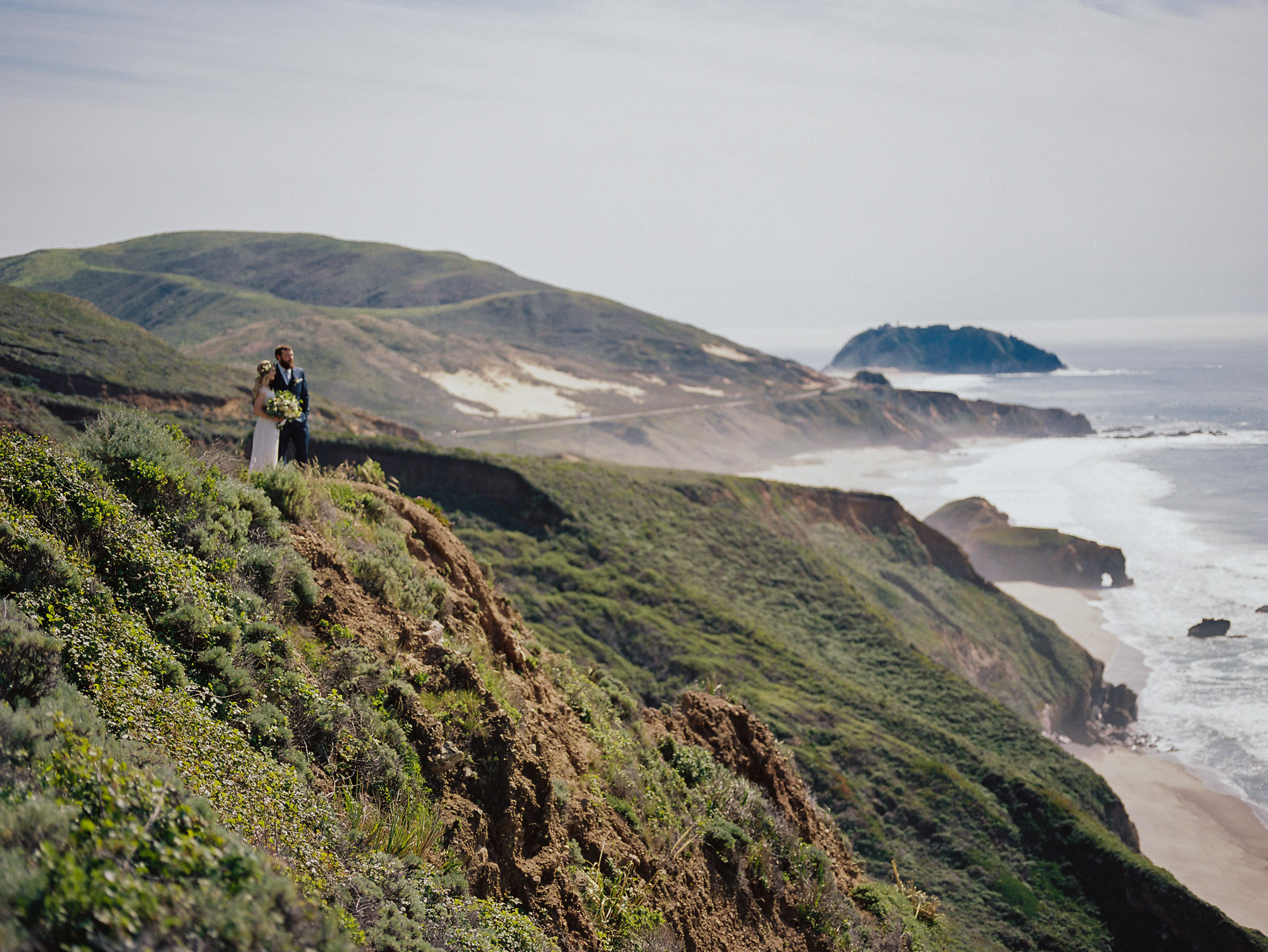 vast ocean scene with couple looking out over pacific ocean bluff off highway 1 in big sur california - fuji 400h medium format film look wedding photography